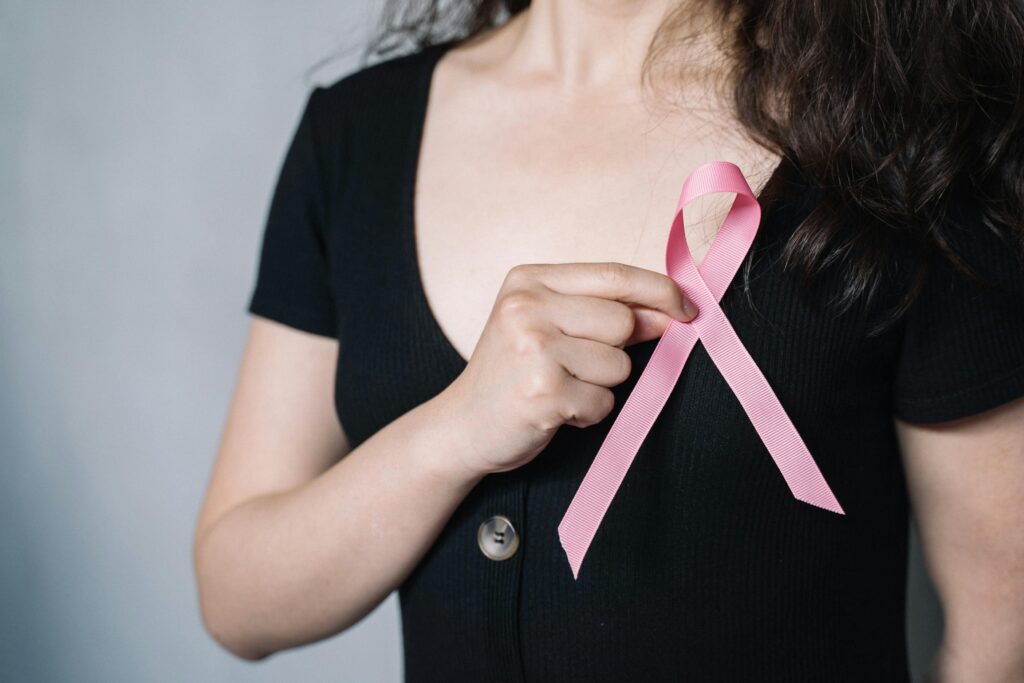 Close-up of a woman holding a pink ribbon symbolizing breast cancer awareness and support.